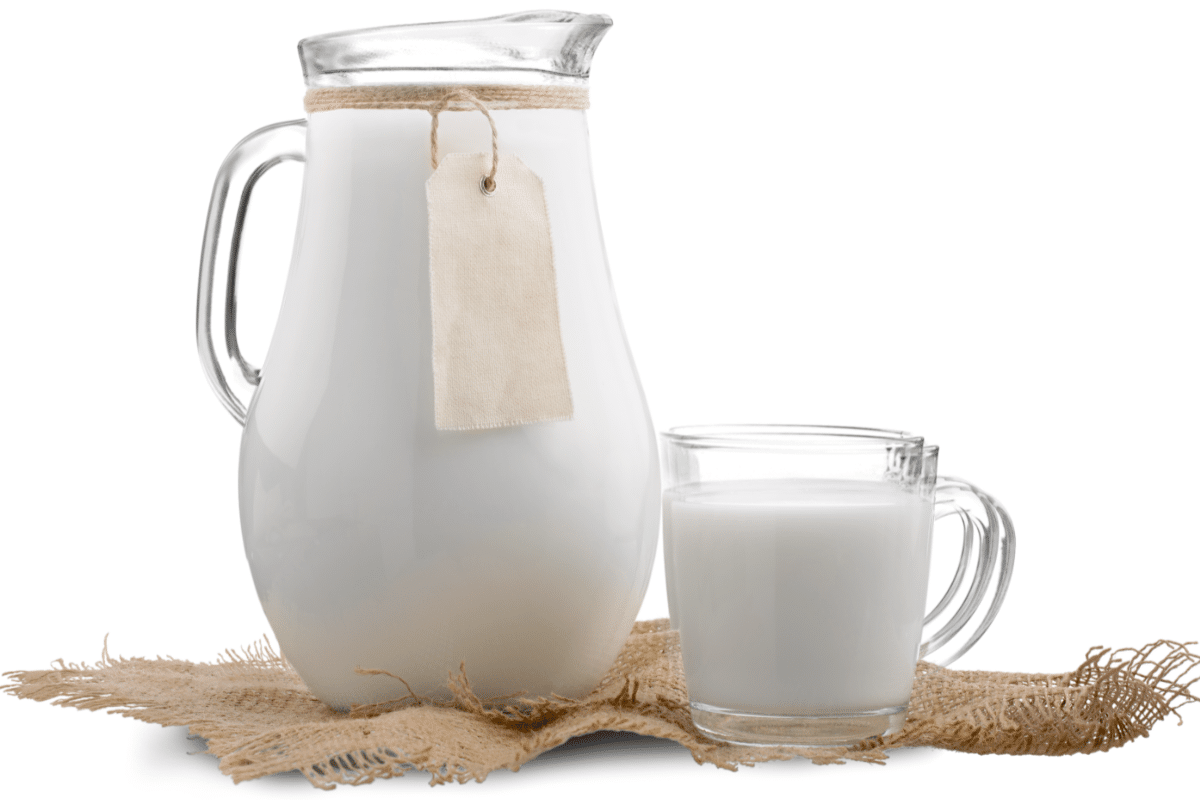 A clear glass pitcher filled with milk is placed on a piece of burlap fabric, accompanied by a glass mug also filled with milk