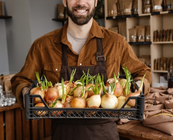 Happy mid aged farmer selling onions at the market indoors, cropped